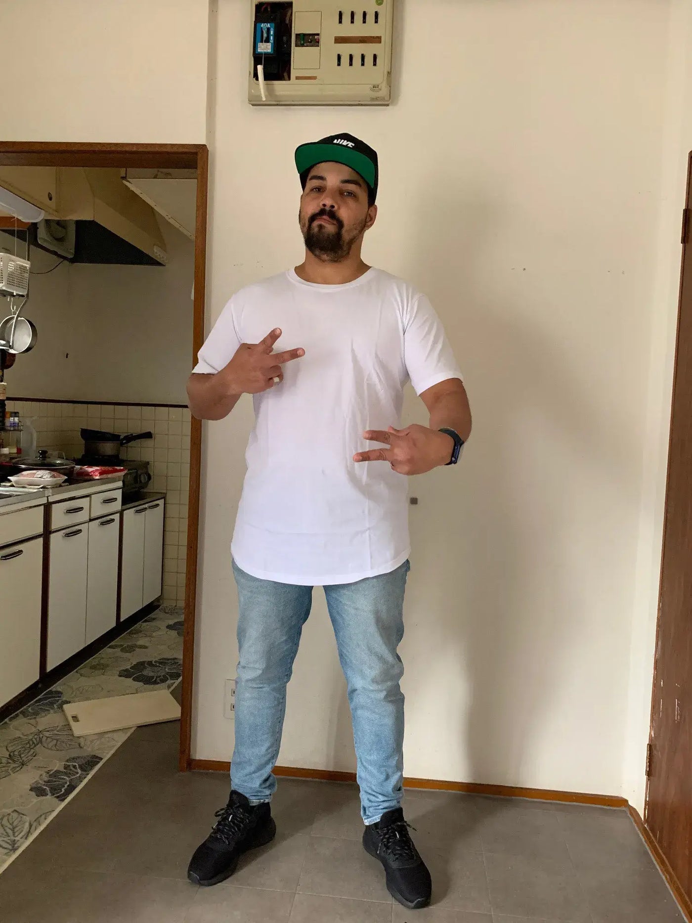 MRMT High Street Mens T Shirt worn by a man in a casual outfit standing indoors with a kitchen in the background.